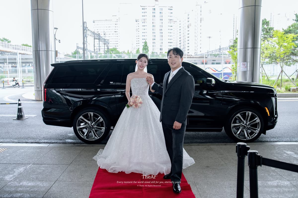 예식장 현관 앞 붉은 카펫 위에 나란히 선 신랑과 신부